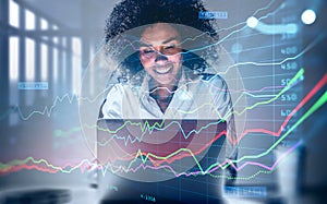 Attractive smiling African American business woman or stock trader analyzing stock graph chart using laptop, Portrait front view