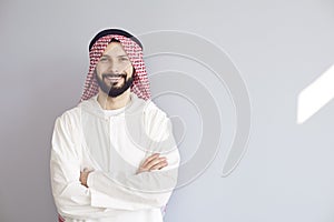 Attractive smiling arab man crossed his arms on a gray background