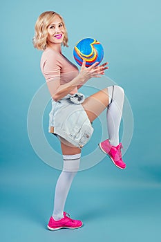 Attractive and smiling blonde woman in a sexy a sports suit ,pink sneakers and gaiters stockings plays with the ball in