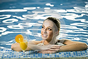 Attractive smiling brunette woman in swimming pool with cocktail