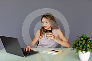 Attractive smiling business woman sitting at office desk, holding a cup of coffee relaxing and looking away