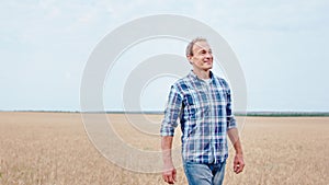 Attractive and smiling farmer walking through the young wheat field he enjoying the moment