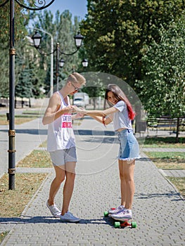 An attractive smiling fellow teaching a girl riding on a longboard in a park on a natural blurred background.