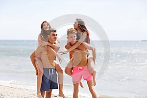 Attractive smiling fellows holds beautiful girls on a seashore on a natural blurred background.