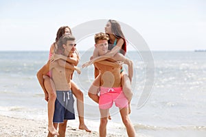 Attractive smiling fellows holds beautiful girls on a seashore on a natural blurred background.