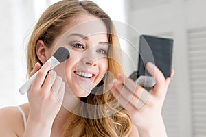 attractive smiling girl applying compact powder with brush and looking photo