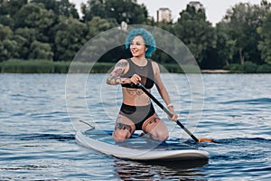 attractive smiling girl with blue hair sitting on paddle board