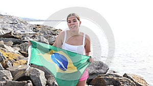 Attractive smiling girl holding Brazilian flag on the seashore on a sunny day