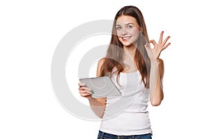 Attractive smiling girl in white shirt using tablet showing okay sign. Woman with tablet pc, on white background