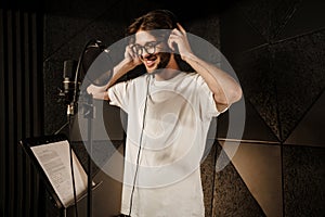 Attractive smiling guy happily wearing headphones recording new song in modern studio