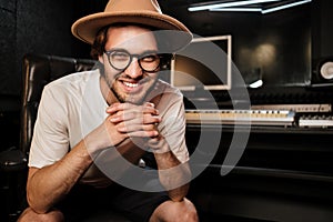 Attractive smiling guy joyfully posingon camera in sound recording studio. Young stylish musician happily working in