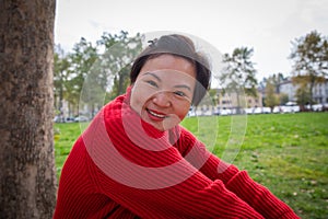 Attractive smiling middle aged chinese woman sitting on the grass at the park