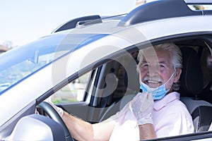 Attractive smiling senior man with protective gloves driving silver car moves away from face mask against coronavirus - new normal