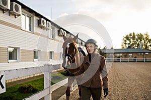 Attractive smiling woman equestrian walking horse in outdoor paddock