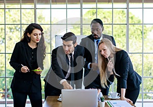 Attractive smiling young adult caucasian businessman leader discussing with the multiracial colleagues. CEO looking and pointing