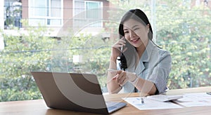 Attractive smiling young asian business woman relaxing at office, working on laptop computer, talking on mobile phone