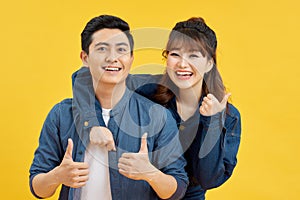 Attractive smiling young Asian couple being happy and amazed isolated on yellow studio background