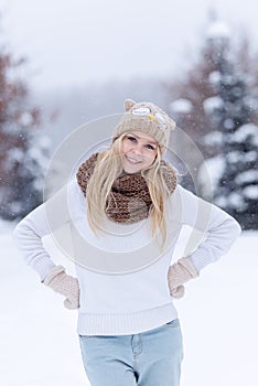 Attractive smiling young blonde girl walking in winter forest. Pretty woman in wintertime outdoor. Wearing winter clothes.