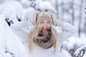 Attractive smiling young blonde girl walking in winter forest. Pretty woman in wintertime outdoor. Wearing winter clothes.