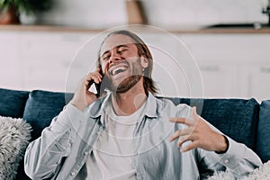 attractive smiling young man talking on mobile phone wearing casual clothes sitting on a couch at the living room