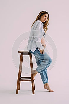 Attractive young pregnant woman sitting on a chair isolated over white background, showing peace gesture