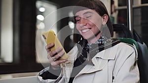 Attractive smiling young woman in public transport using a mobile phone. She is texting, checking mails, chats or the