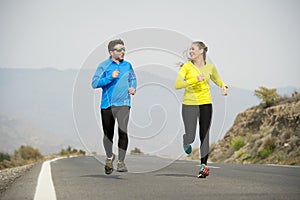 Attractive sport couple man and woman running together on asphalt road mountain landscape