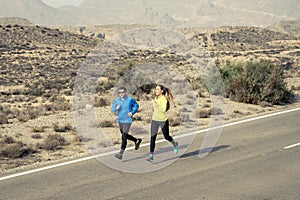 Attractive sport couple man and woman running together on desert asphalt road mountain landscape