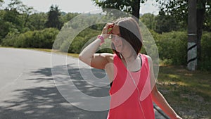 Attractive sportive girl enjoying her walking in park. Young woman in headphones dancing. Cute girl in pink shirt smiling. Beautif