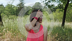 Attractive sportive girl in pink top with headphones listening music on smartphone. Slim brunette girl dancing in park. Young girl