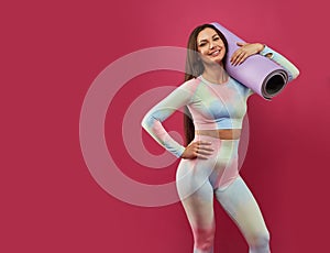 Attractive sportswoman posing with yoga mat on shoulder.