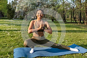 Attractive sporty black woman doing warming up stretching exercses on yoga mat at urban park, copy space