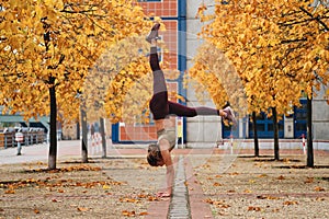 Attractive sporty girl standing on hands during yoga practice on autumn city street