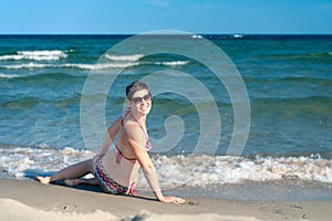 Attractive sporty short haired woman in her thirties, wearing bikini, sitting on a beach close to the sea, looking back