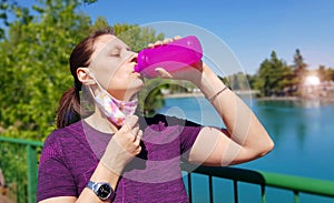 Attractive sporty woman drinking water from a bottle after jogging or running at park