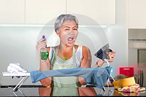 Attractive and stressed Asian middle aged lady ironing at home kitchen desperate and overwhelmed feeling unhappy in helpless face