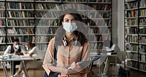 Attractive student girl wear protective face mask posing in library