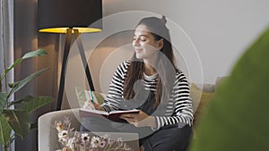 Attractive student woman at home making notes and working on laptop in cozy living room