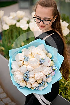 Attractive stylish brunette girl in black suit holds bouquet of white fragnant peonies formed with blue packing paper