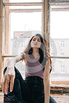 Attractive stylish caucasian woman with long brunette hair sitting on windowsill in living room