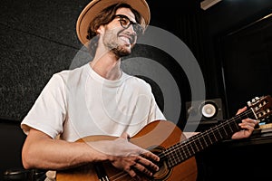 Attractive stylish man singing and playing on a guitar in studio. Young musician recording new song in modern studio