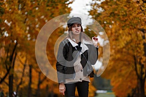 Attractive stylish model of a young woman in fashionable clothes in an elegant hat with a leather handbag posing in the park on an
