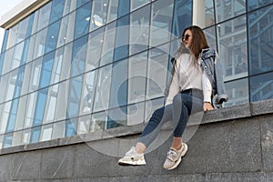 Attractive stylish woman resting on city street. Young woman in sunglesses in youth clothing on the city street