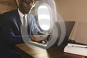 Attractive and successful African American businessman with glasses working on a laptop while sitting in the chair of