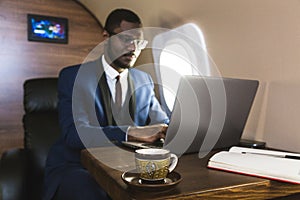 Attractive and successful African American businessman with glasses working on a laptop while sitting in the chair of