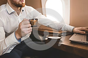 Attractive and successful businessman drinking coffee and working behind a laptop while sitting in a chair of his