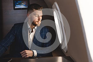 Attractive and successful businessman in an expensive suit working sitting in the chair of his private jet.