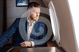 Attractive and successful businessman in an expensive suit working sitting in the chair of his private jet.