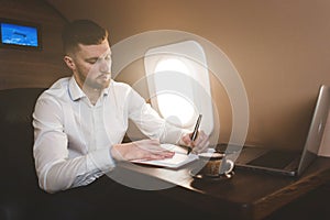 Attractive and successful businessman in a white shirtt working sitting in the chair of his private jet.