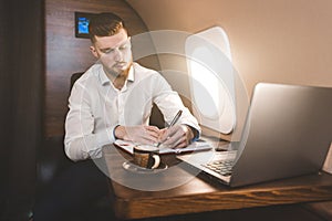 Attractive and successful businessman in a white shirtt working sitting in the chair of his private jet.